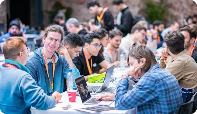 Group of people sit at long table outside at Flare event, some on their laptops